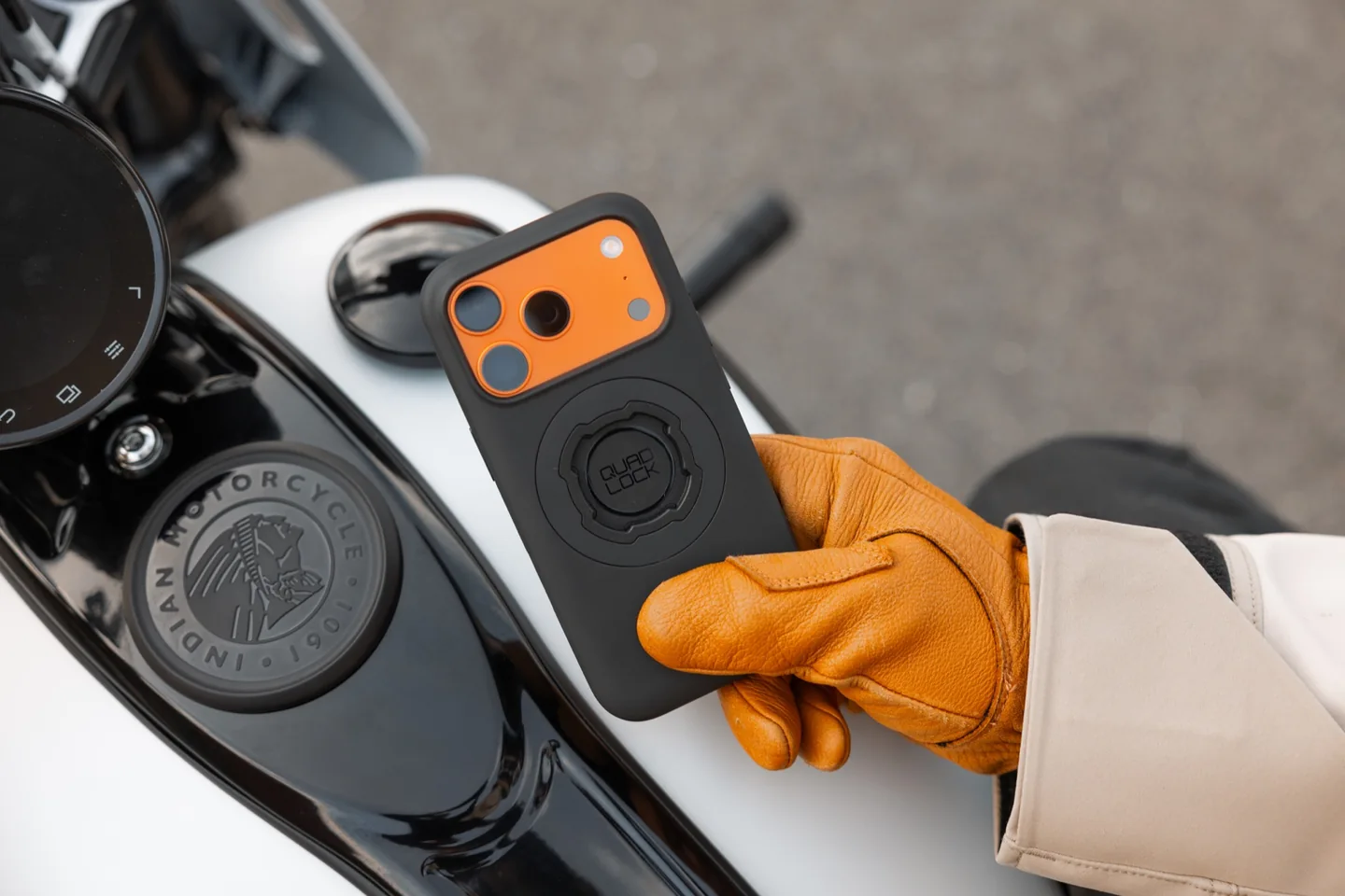 A rider holding a phone in a Quad Lock case beside a motorcycle.